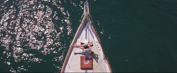 Movie still from “Dead Calm” (1989), directed by Phillip Noyce – A woman laying on the bow of a sail boat in the ocean; Wide shot, Overhead angle