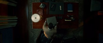 Movie still from “Dead Man Down” (2013), directed by Niels Arden Oplev – A man sitting at a desk holding a laptop; Medium shot, High angle