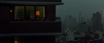 Movie still from “Dead Man Down” (2013), directed by Niels Arden Oplev – A person standing on a balcony looking out of a window; Extreme Wide shot, Over the shoulder angle