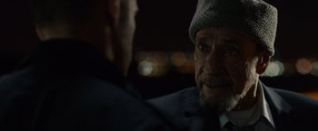 Movie still from “Dead Man Down” (2013), directed by Niels Arden Oplev – A man wearing a hat looking at another man in a suit; Close Up shot, Over the shoulder angle