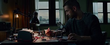Movie still from “Dead Man Down” (2013), directed by Niels Arden Oplev – A man sitting at a desk working on a project; Medium shot, Low angle