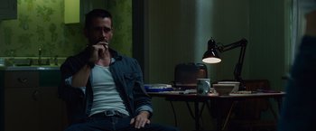 Movie still from “Dead Man Down” (2013), directed by Niels Arden Oplev – A man sitting at a table in a dark room; Medium shot, Low angle