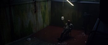 Movie still from “Dead Man Down” (2013), directed by Niels Arden Oplev – A man sitting on a chair in a room; Wide shot, Overhead angle