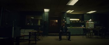 Movie still from “Dead Man Down” (2013), directed by Niels Arden Oplev – A man sitting on a chair in a dark room; Wide shot, Low angle