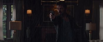 Movie still from “Dead Man Down” (2013), directed by Niels Arden Oplev – A man is holding a gun in a dark room; Medium shot, Over the shoulder angle