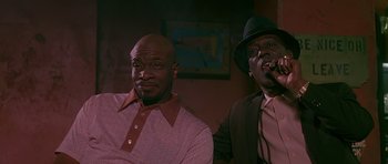 Movie still from “Dead Presidents” (1995), directed by Albert Hughes – A couple of men sitting next to each other in front of a painting; Medium shot, Low angle