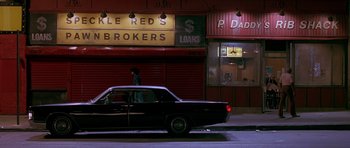 Movie still from “Dead Presidents” (1995), directed by Albert Hughes – A car parked on the side of the road in front of a building; Wide shot, Low angle