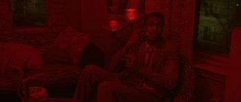 Movie still from “Dead Presidents” (1995), directed by Albert Hughes – A man sitting on a couch holding a cigarette; Medium shot, High angle
