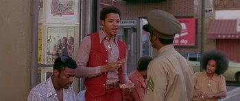 Movie still from “Dead Presidents” (1995), directed by Albert Hughes – A man in a red vest is talking to a man in a brown jacket; Medium shot, Low angle