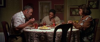 Movie still from “Dead Presidents” (1995), directed by Albert Hughes – A group of people sitting at a dinner table eating food; Medium shot, High angle