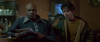 Movie still from “Dead Presidents” (1995), directed by Albert Hughes – Two men standing next to each other in front of a television; Medium shot, Low angle