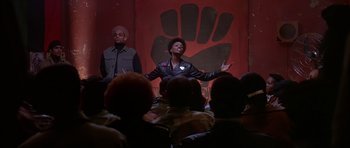 Movie still from “Dead Presidents” (1995), directed by Albert Hughes – A man in a leather jacket is speaking to a crowd; Medium shot, Low angle