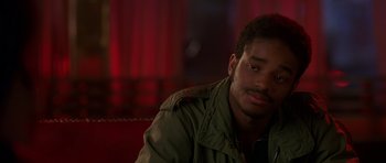 Movie still from “Dead Presidents” (1995), directed by Albert Hughes – A man sitting on a couch in front of a red curtain; Close Up shot, Over the shoulder angle