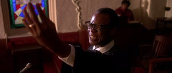 Movie still from “Dead Presidents” (1995), directed by Albert Hughes – A man in a suit and glasses is smiling for the camera; Close Up shot, Low angle