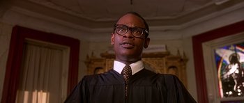 Movie still from “Dead Presidents” (1995), directed by Albert Hughes – A man wearing a robe and glasses in a room; Close Up shot, Low angle
