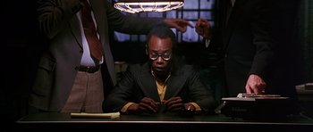 Movie still from “Dead Presidents” (1995), directed by Albert Hughes – A man sitting at a table in front of a lamp; Medium shot, Low angle