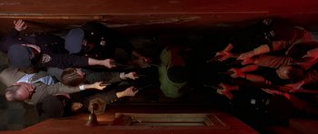 Movie still from “Dead Presidents” (1995), directed by Albert Hughes – A group of people standing in a dark room holding guns; Wide shot, Overhead angle