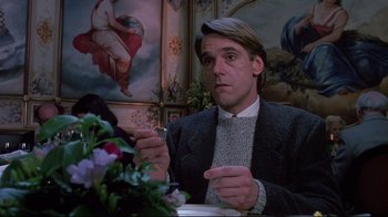 Movie still from “Dead Ringers” (1988), directed by David Cronenberg – A man sitting in front of a table holding a fork; Medium shot, Low angle