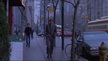 Movie still from “Dead Ringers” (1988), directed by David Cronenberg – A man walking down the street in a suit; Wide shot, Low angle