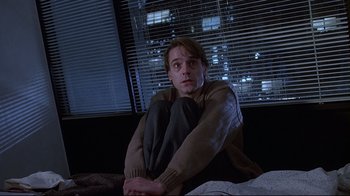 Movie still from “Dead Ringers” (1988), directed by David Cronenberg – A man sitting on a bed in front of a window at night; Medium shot, Low angle