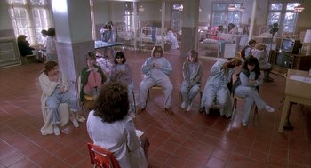 Movie still from “Death Becomes Her” (1992), directed by Robert Zemeckis – A group of people sitting in a circle in a room; Wide shot, Overhead angle
