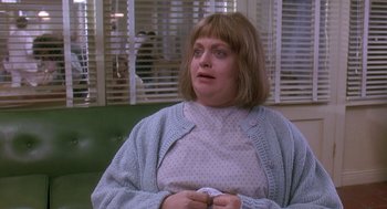 Movie still from “Death Becomes Her” (1992), directed by Robert Zemeckis – A woman sitting in front of a window holding a paper napkin; Medium shot, Over the shoulder angle