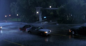 Movie still from “Death Becomes Her” (1992), directed by Robert Zemeckis – A couple of cars driving down a street in the rain; Extreme Wide shot, High angle