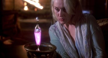 Movie still from “Death Becomes Her” (1992), directed by Robert Zemeckis – A woman sitting in front of a table looking at a bottle; Close Up shot, High angle