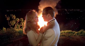 Movie still from “Death Becomes Her” (1992), directed by Robert Zemeckis – A man and a woman standing next to each other in front of a fire; Medium shot, Low angle