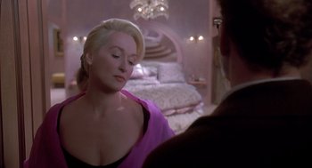 Movie still from “Death Becomes Her” (1992), directed by Robert Zemeckis – A woman in a pink dress is talking to a man in a suit; Medium shot, Over the shoulder angle