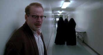 Movie still from “Death Becomes Her” (1992), directed by Robert Zemeckis – A man with glasses standing in a hallway with two nuns; Medium shot, Over the shoulder angle