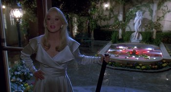 Movie still from “Death Becomes Her” (1992), directed by Robert Zemeckis – A woman in a white dress holding a sword in front of a fountain; Medium shot, Over the shoulder angle