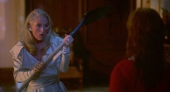Movie still from “Death Becomes Her” (1992), directed by Robert Zemeckis – A woman holding a large black object in her hand; Medium shot, Over the shoulder angle