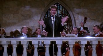 Movie still from “Death Becomes Her” (1992), directed by Robert Zemeckis – A man in a tuxedo is speaking to a crowd; Medium shot, Low angle