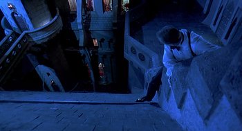 Movie still from “Death Becomes Her” (1992), directed by Robert Zemeckis – A man standing on the side of a building at the top of a flight of stairs; Wide shot, Overhead angle