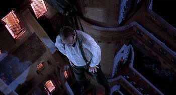 Movie still from “Death Becomes Her” (1992), directed by Robert Zemeckis – A man in a white shirt and black tie standing in a room; Wide shot, Overhead angle
