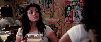 Movie still from “Death Proof” (2007), directed by Quentin Tarantino – A woman sitting at a table in front of posters; Close Up shot, Low angle