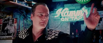 Movie still from “Death Proof” (2007), directed by Quentin Tarantino – A man in a black and white shirt is in front of a neon sign; Close Up shot, Low angle