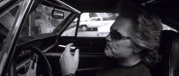 Movie still from “Death Proof” (2007), directed by Quentin Tarantino – A man smoking a cigarette while sitting in the passenger seat of a car; Close Up shot, Low angle