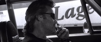 Movie still from “Death Proof” (2007), directed by Quentin Tarantino – A black and white photo of a man smoking a cigarette; Close Up shot, Low angle