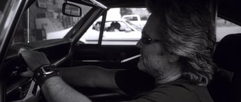 Movie still from “Death Proof” (2007), directed by Quentin Tarantino – A man sitting in the drivers seat of a car while smoking a cigarette; Close Up shot, Over the shoulder angle
