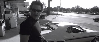 Movie still from “Death Proof” (2007), directed by Quentin Tarantino – A black and white photo of a man standing in front of a car; Medium shot, Low angle
