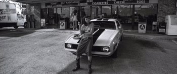 Movie still from “Death Proof” (2007), directed by Quentin Tarantino – A black and white photo of a woman standing in front of a car; Wide shot, Low angle