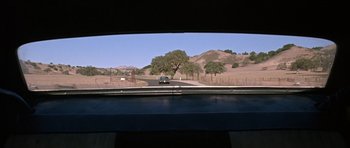 Movie still from “Death Proof” (2007), directed by Quentin Tarantino – A car driving down a road near a field; Wide shot, Low angle