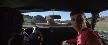 Movie still from “Death Proof” (2007), directed by Quentin Tarantino – A woman is driving a car while a man is sitting in the driver's seat; Medium shot, Over the shoulder angle