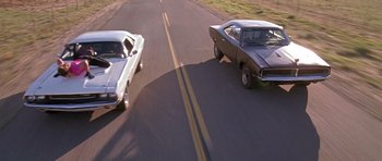Movie still from “Death Proof” (2007), directed by Quentin Tarantino – Two cars on a road with a grass field in the background; Wide shot, Overhead angle