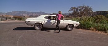 Movie still from “Death Proof” (2007), directed by Quentin Tarantino – A woman in a pink shirt is standing next to a white car; Wide shot, High angle