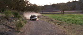 Movie still from “Death Proof” (2007), directed by Quentin Tarantino – A car driving down a dirt road near a field; Extreme Wide shot, High angle