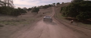 Movie still from “Death Proof” (2007), directed by Quentin Tarantino – A car driving down a dirt road in the middle of the day; Wide shot, High angle