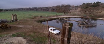 Movie still from “Death Proof” (2007), directed by Quentin Tarantino – A white car parked in front of a body of water; Extreme Wide shot, High angle